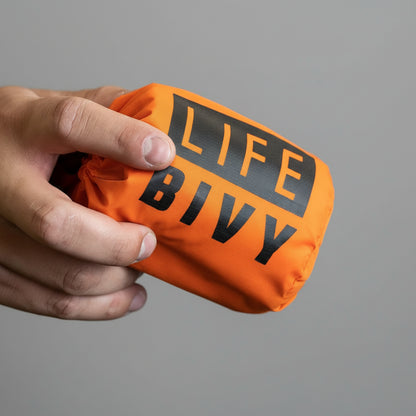 Orange emergency thermal bivy with high-visibility design, reflective survival sleeping bag for cold weather emergencies and outdoor safety held by hand .
