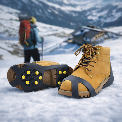 Pair of yellow hiking boots with ice cleats  on a snowy background with a hiker and mountain house.
