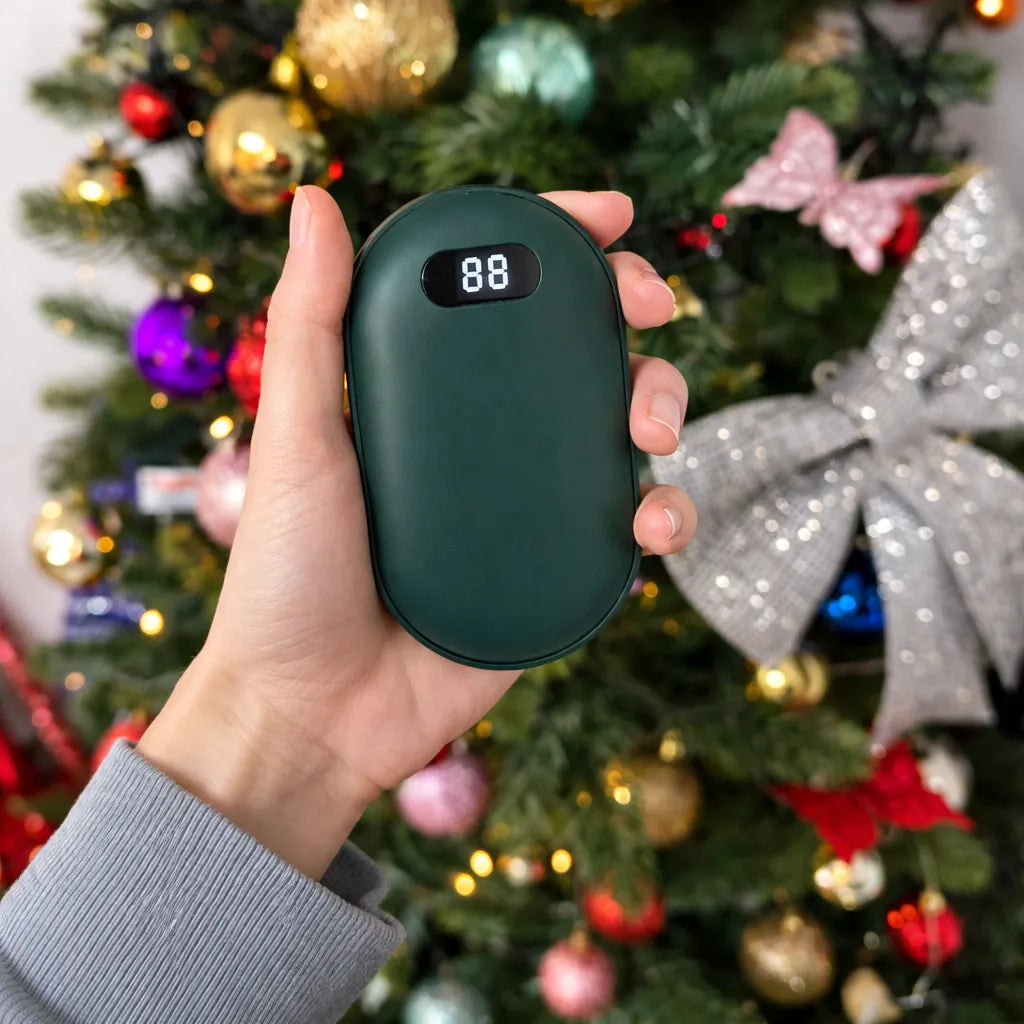 Hand holding a green portable hand warmer in front of a decorated Christmas tree by treknest